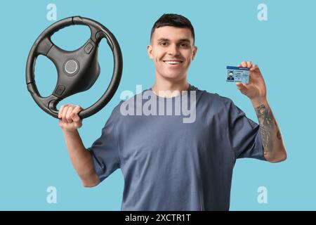Young happy man holding driver license and steering wheel on blue background Stock Photo