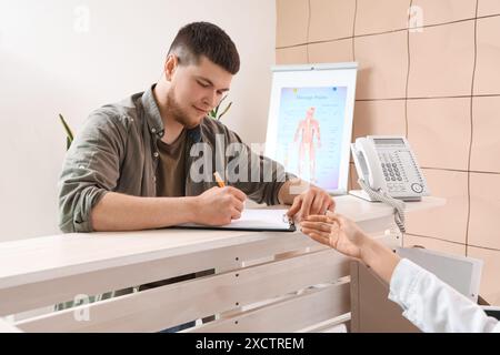 Young man filling out form at reception desk in clinic Stock Photo