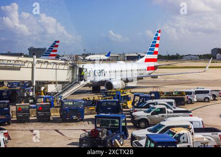 View of Miami airport runway with cargo trucks and American Airlines plane connected to jet bridge for passenger boarding. Miami. USA. Stock Photo