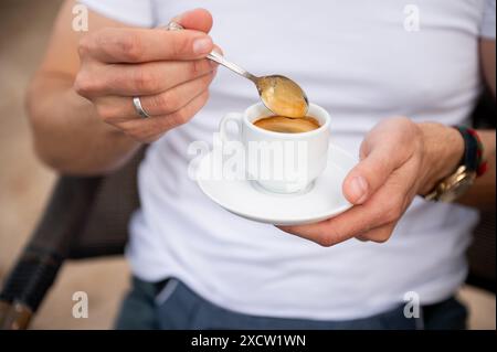 Close-up of a man stirring a cup of espresso with a spoon, creating a cozy and relaxing moment. Perfect for depicting coffee culture and mornings. Stock Photo