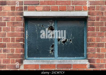 Weathered window glass with sustained damage and impact marks from stones, surrounded by a red brick wall, England, UK Stock Photo