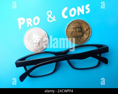 Golden bitcoin and silver ethereum glasses with text PRO AND CONS on blue background. Stock Photo