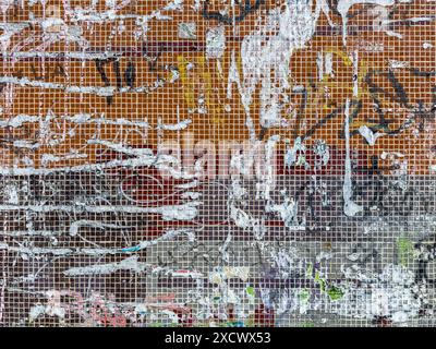 weathered wall of small ceramic tiles with torn pieces of paper and graffiti. urban background. Stock Photo
