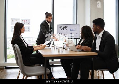 Businessman handing out paper tasks during team meeting Stock Photo