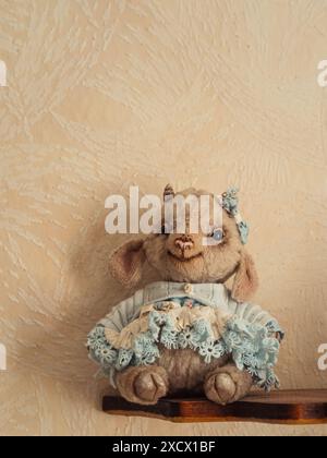 Charming Teddy Lamb: A vertical close-up shot of a cute Teddy Lamb wearing a blue dress, seated on a shelf. Stock Photo