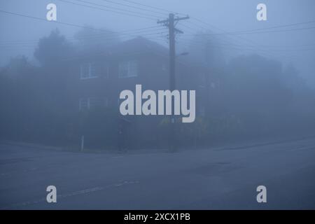 A corner block of flats at dusk, streetlight, power lines and power pole in heavy fog on suburban Katoomba street, Blue Mountains Stock Photo