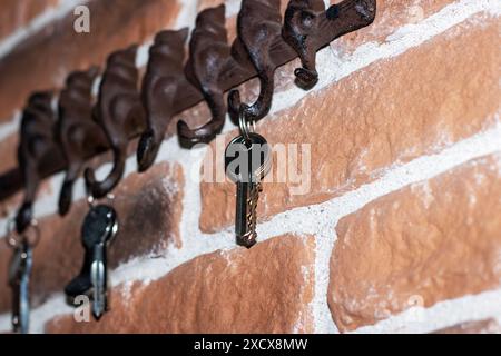 A group of keys are dangling from a hook mounted on a brick wall. The wall is built using bricks and serves as a secure spot for the keys Stock Photo