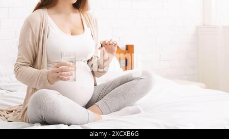 Pregnant Woman Sitting on Bed With Glass Water and Pill Stock Photo