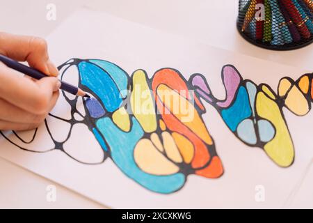 Lady paints over a drawing on a white sheet with colored pencils Stock Photo