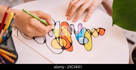 Lady paints over a drawing on a white sheet with colored pencils Stock Photo