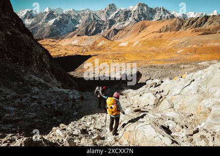 Two trekkers trekking in Himalayas mountains through Chola pass hold use rope to Gokyo Ri. Nepalese male guide leading tourist client in Sagarmatha na Stock Photo