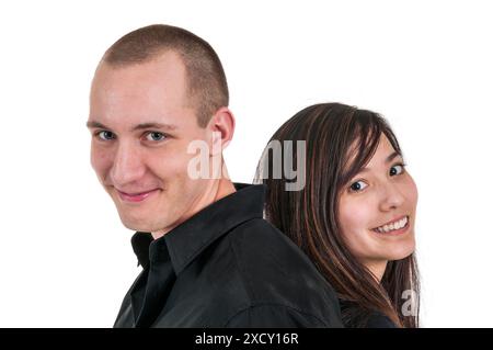 Side head and shoulder view of a young heterosexual couple of Caucasian and Asian descent standing back to back in front of a white background. Stock Photo