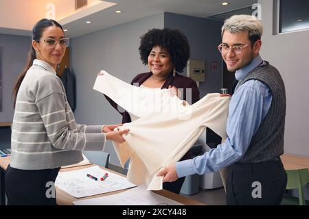 The Team of two Young Latin Women and one Man are looking at the camera smiling while working, are standing in the office happily discussing type of f Stock Photo