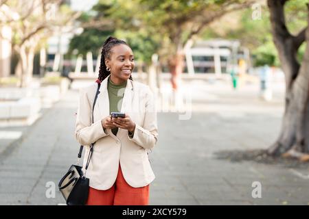Confident Black Woman Entrepreneur Walking Outdoors with Mobile Phone Stock Photo