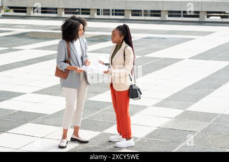 Two Black Businesswomen Discussing Documents Outside Modern Office Building Stock Photo