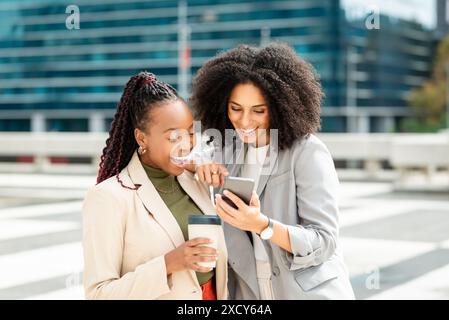 Two Businesswomen Discussing Project Ideas on Smartphone Outside Office Building Stock Photo