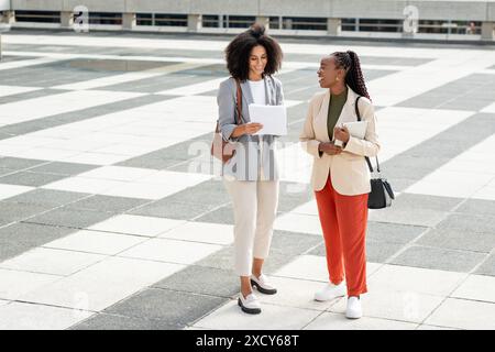Smiling Black Businesswomen Discussing Documents Outdoors in Professional Attire Stock Photo