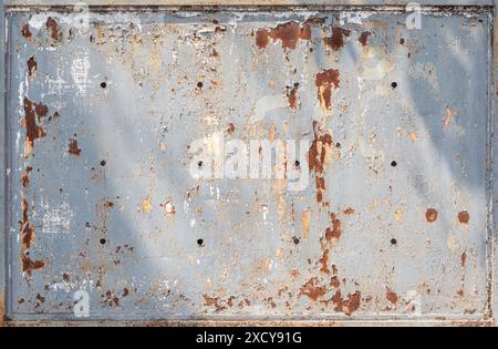 Front view of a weathered, aged & dirty metal plate painted in light gray. Paint is partly peeled off revealing rust. Abstract background, copy space. Stock Photo