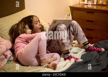 2 sisters are reading a great book together. They are amazed as the older one tells her little sister the great story that lies inside that great book Stock Photo