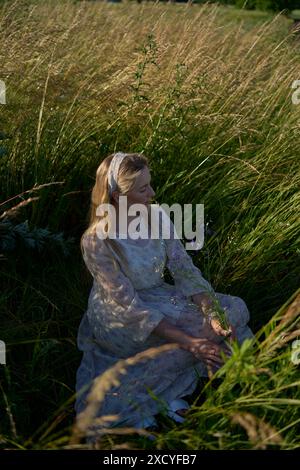 a portrait of a young blonde woman in a pastel chiffon dress in a field of golden grass Stock Photo