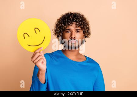 Photo of sad depressed stressed guy wear stylish blue clothes hold yellow smiley isolated on beige color background Stock Photo