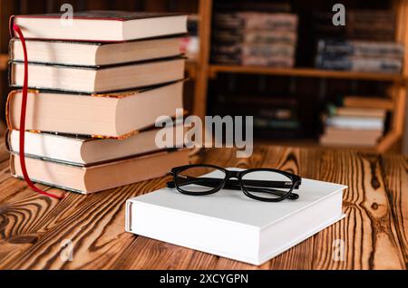 Black glasses lying on a white book next to old books against the background of bookshelves Stock Photo