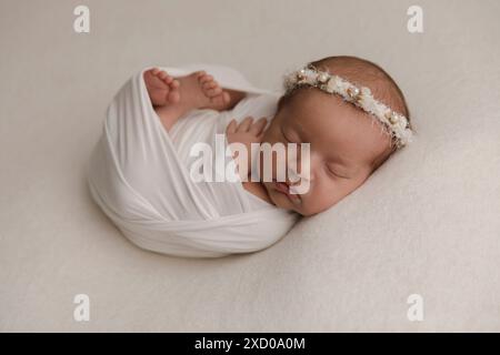 Top view of a newborn baby sleeping on a bed under beige blanket and a bendable headband flower on her head. Copy space. Newborn baby care concept. Stock Photo