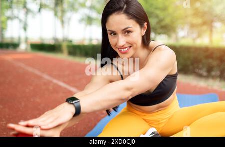 Happy fit young woman doing stretching exercises as she sits on an athletics track warming up before a workout in a health and fitness concept. High q Stock Photo