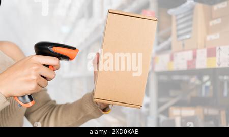 A woman is holding a barcode scanner and looking at a cardboard box. Concept of productivity and efficiency, as the woman is using technology to compl Stock Photo