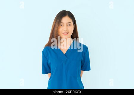 A woman in a blue scrubs shirt is smiling. She is a nurse or a doctor on blue isolated background. Stock Photo