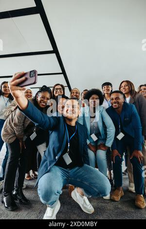 Friendly group of happy colleagues taking a group selfie photo at a corporate event, showing teamwork and camaraderie. Stock Photo