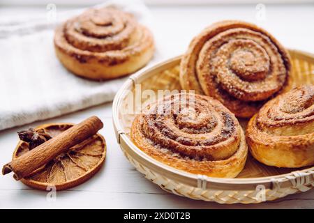 Freshly baked homemade cinnamon rolls with sugar on top in basket in home kitchen on white table, cinnamon stick for decoration. Selective focus. Stock Photo