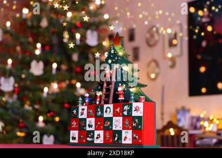 painted advent calendar made of wood with stylised Christmas Tree, tiny figures and drawers standing on a table in the middle of a Christmassy decorat Stock Photo