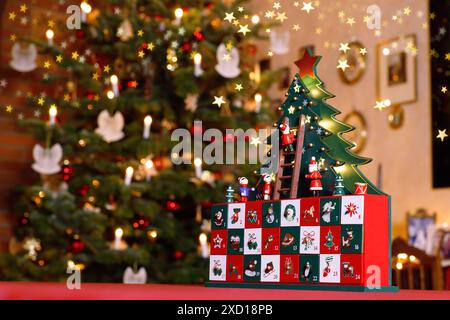 closeup of apainted advent calendar made of wood with stylised Christmas Tree, tiny figures and drawers in front of blurred Christmassy illuminated ro Stock Photo