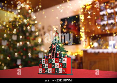 closeup of apainted advent calendar made of wood with stylised Christmas Tree, tiny figures and drawers in front of blurred Christmassy illuminated ro Stock Photo