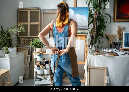 Woman painter tying apron getting ready for creative work. Female artist at art workshop Stock Photo