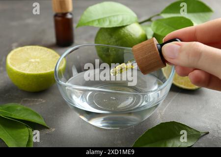 Woman dripping essential oil from pipette into bowl at gray table, closeup Stock Photo