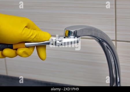 A plumber wearing yellow rubber gloves changes the faucet aerator. Regular repairs and replacement of water pipes Stock Photo