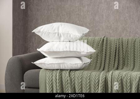Stack of soft white pillows on sofa and blanket indoors Stock Photo