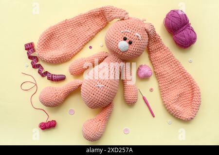 Crocheted rabbit toy, yarn ball and measuring tape on yellow background Stock Photo