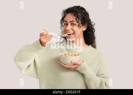 Beautiful young woman eating tasty cereal rings on light background Stock Photo