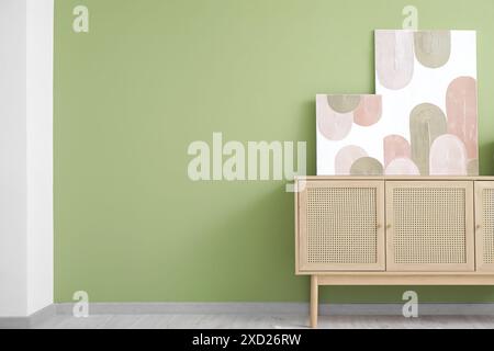 Wooden chest of drawers and beautiful pictures on green wall in room Stock Photo