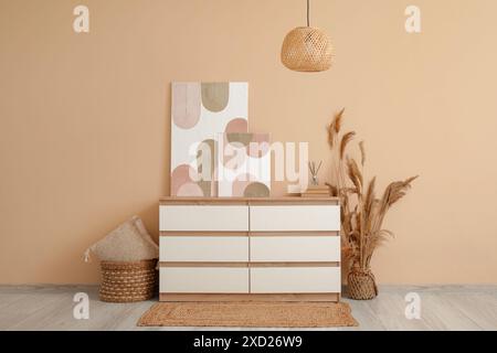 Chest of drawers, pampas grass, lamp and beautiful pictures on beige wall in room Stock Photo