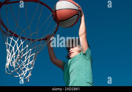 Kid basketball player makes slam dunk. Active child enjoying outdoor game with basketball. Stock Photo