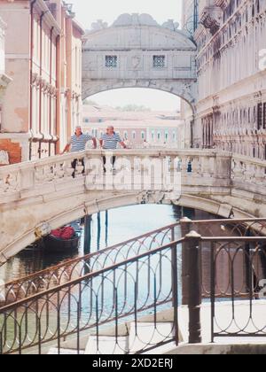 Venice, Italy - June 20th 2021 Two gondoliers taking a break from punting tourists along a venice canal, posing on Sighs bridge with the bridge of sig Stock Photo