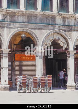 Venice, Italy - June 20th 2020 Couple is walking past a closed restaurant with stacked chairs in a square in venice, italy during lockdown Stock Photo