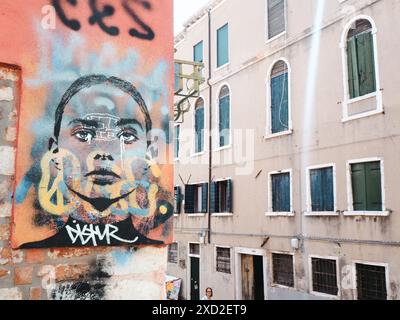 Venice, Italy - June 20th 2024 Large street art painting depicting a sad girl crying on a brick wall with a senior woman walking in a narrow street in Stock Photo