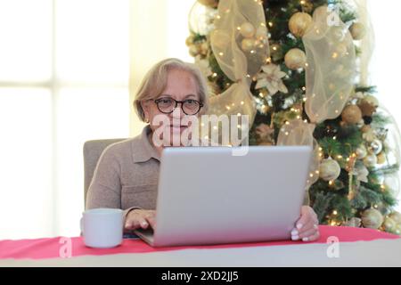 Older woman drinks a coffee while using the computer Stock Photo