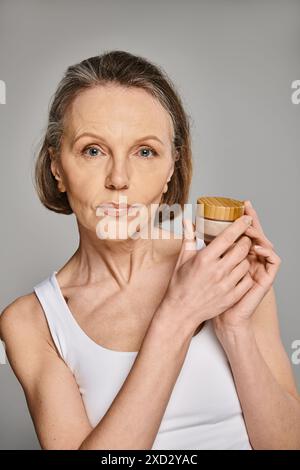A mature attractive woman in comfy attire holds a jar of cream gracefully. Stock Photo