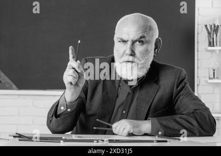 Serious professor. Education and knowledge concept. Elderly professor, teacher on blackboard. Senior professor, teacher in classroom. Funny professor Stock Photo